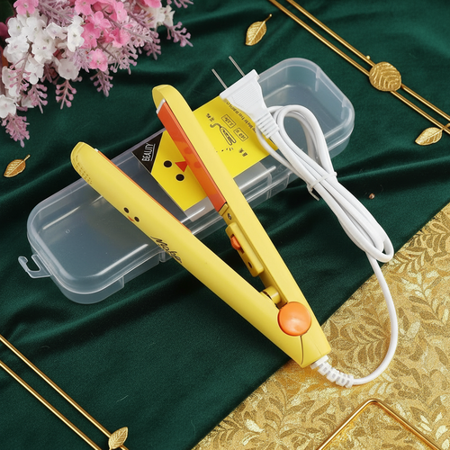 Yellow hair straightener on a green and gold fabric background with flowers.