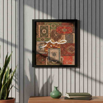 Framed artwork with a patchwork design and Arabic text on a wall with a wooden shelf below.
