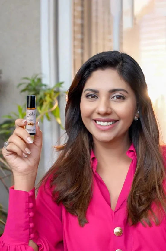 Woman holding a small bottle with a dropper, possibly an essential oil bottle, in a bright indoor setting.